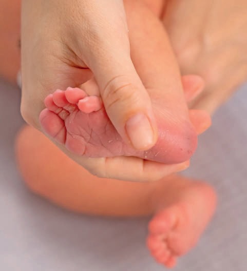 Mère tenant le pied d'un bébé en bas âge, illustrant la douceur et le soin.