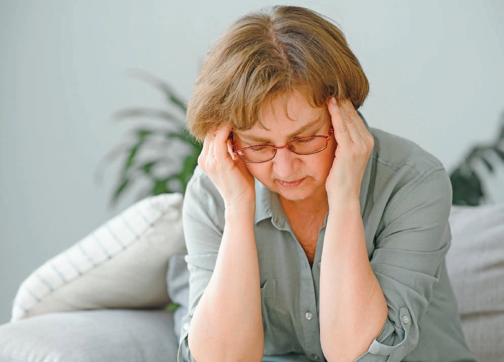 Femme âgée souffrant de douleur chronique, tenant sa tête avec expression de malaise, dans un cadre intérieur calme.