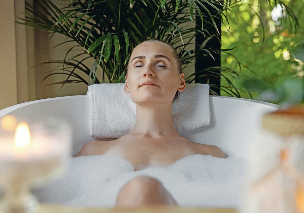 Femme détendue profitant d'un bain chaud dans un spa de bien-être, entourée de plantes vertes, pour une relaxation profonde et un soin du corps.