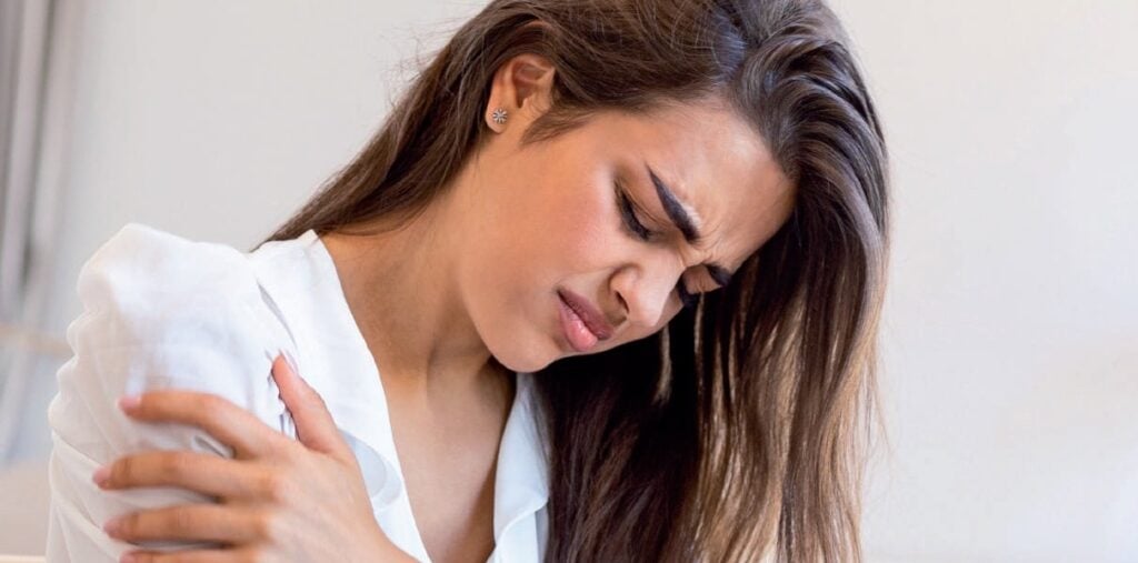 Une femme souffre de douleur à l'épaule, illustrant un problème de santé nécessitant une attention médicale.
