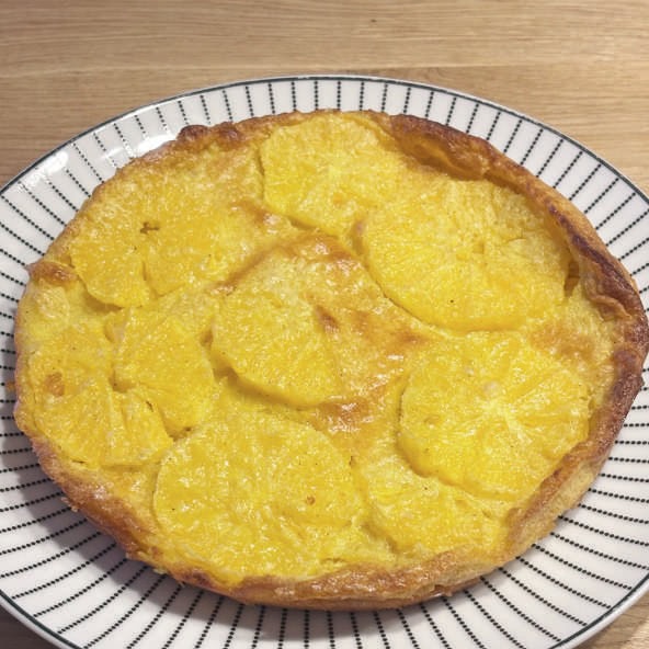 Flan à l'orange doré et appétissant, présenté sur une assiette en bois, mettant en valeur sa texture onctueuse et ses morceaux d'orange fraîche.