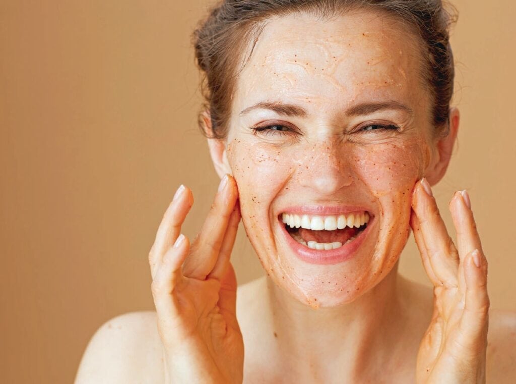 Jeune femme souriante avec une peau claire et éclatante, appliquant un soin facial naturel pour une peau saine et radieuse.
