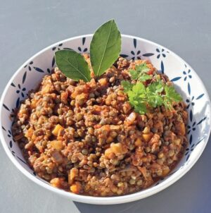 Ragoût de lentilles et légumes bio dans un bol blanc avec des herbes fraîches, idéal pour une alimentation saine et végétarienne.