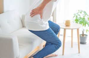 Femme souffrant de douleur au bas du dos en position assise, illustrant un problème de lombalgie ou de mal de dos.