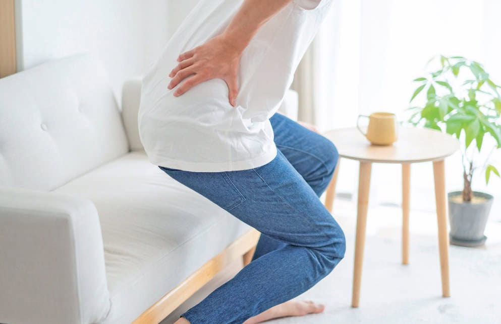 Femme souffrant de douleur au bas du dos en position assise, illustrant un problème de lombalgie ou de mal de dos.