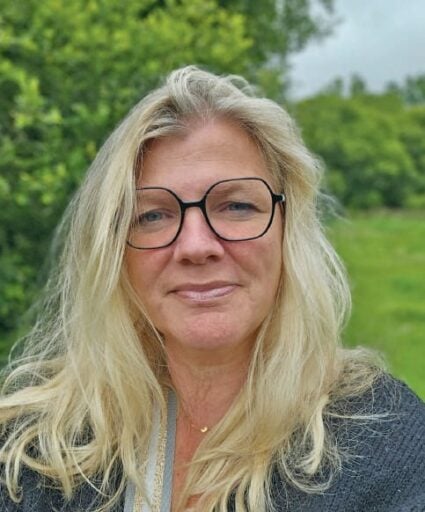 Femme avec lunettes, souriant légèrement, en extérieur avec verdure, illustrant le sujet des étourdissements posturaux-perceptifs persistants (PPPD).