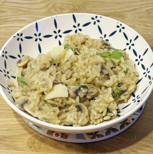 Risotto crémeux aux champignons, garniture fraîche avec herbes aromatiques dans un bol traditionnel. Recette végétarienne, parfaite pour un repas réconfortant et équilibré.