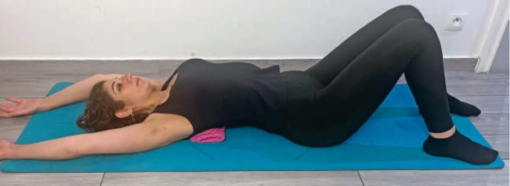 Allongée sur un tapis de yoga, femme pratiquant un étirement ou exercice de relaxation pour la santé et le bien-être, dans un environnement intérieur calme et lumineux.